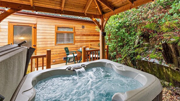 Een houten chalet met een hottub, een houten terras en een muur begroeid met groen.