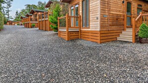 Een rij houten hutten met een grindpad, houten hekwerk en een heldere lucht.