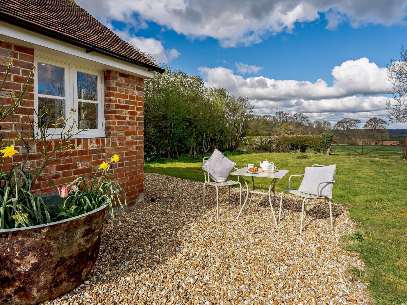 A brick house with a garden patio, a table with chairs, and a view of the countryside.