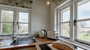Eine Küche mit Spüle, Toaster, Brot auf einem Schneidebrett und großen Fenstern mit Blick ins Grüne.