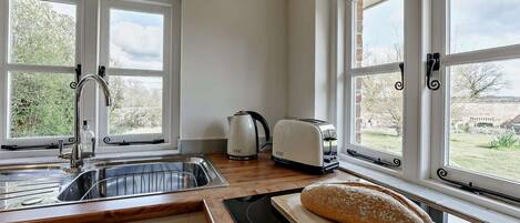 Eine Küche mit Spüle, Toaster, Brot auf einem Schneidebrett und großen Fenstern mit Blick ins Grüne.