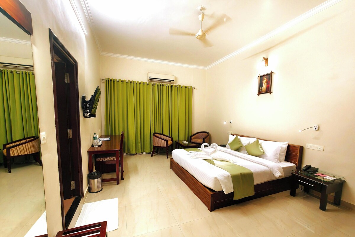 A hotel room with a bed, a desk, a chair, a mirror, and a ceiling fan.