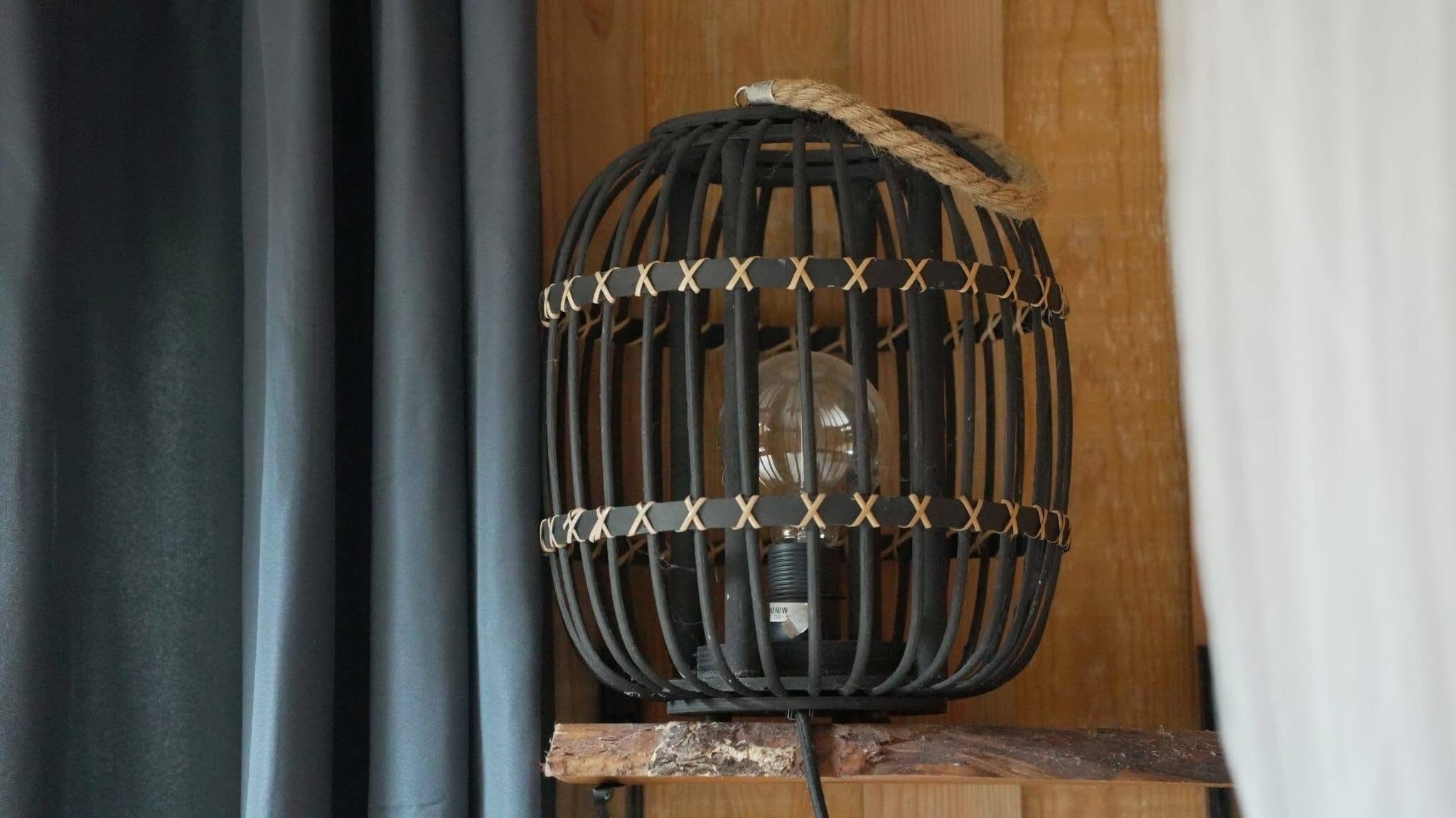 Une lampe noire tressée, avec une ampoule visible et un interrupteur sur une surface en bois.