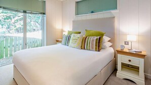 A bedroom with a large bed, two bedside tables, a nightstand, and a window with blinds. - 2 Bed in Conwy (oc-50284) (Ty'n-y-groes)
