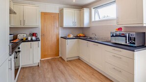 A compact kitchen with white cabinets, a wooden door, a microwave, and a window. - 2 Bed in Conwy (oc-50284) (Ty'n-y-groes)