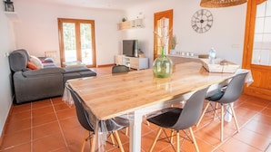 Un vaste espace de vie comprenant une table à manger en bois, un canapé gris et un téléviseur posé sur un meuble blanc.