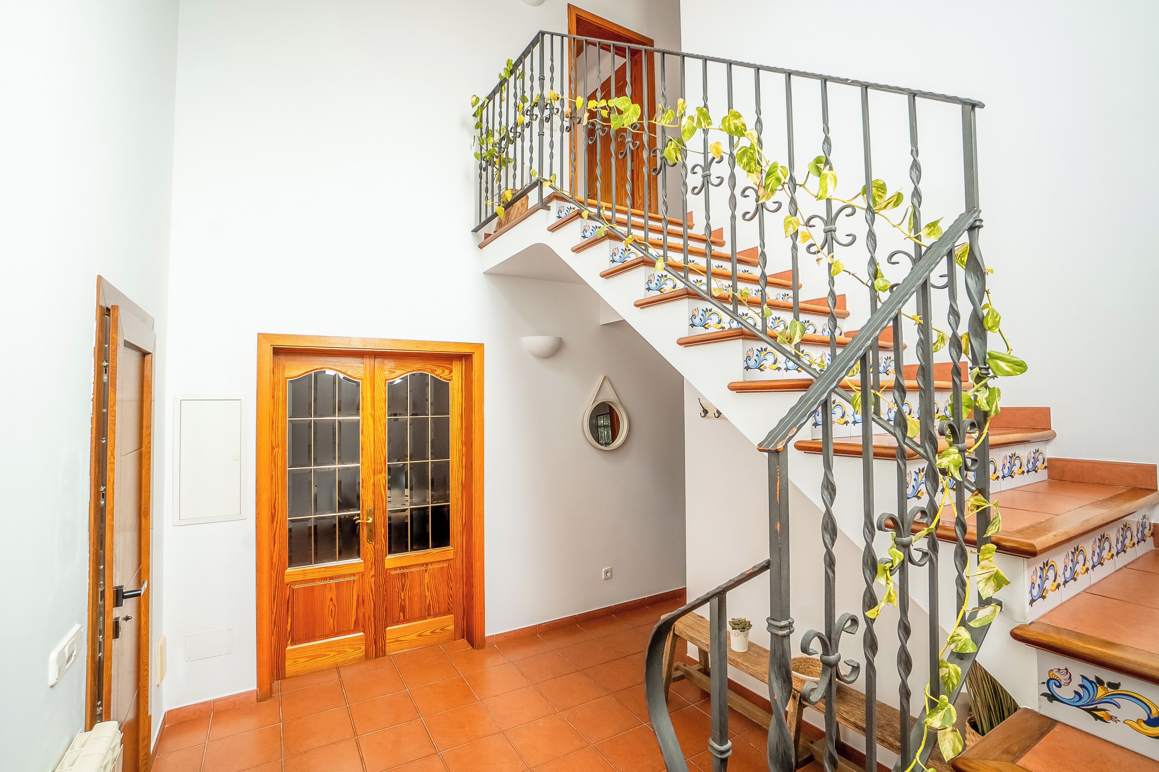 Un escalier en colimaçon orné de rampes en métal ouvragé et une porte en bois dotée de panneaux de verre.