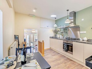 A modern kitchen with a dining area, featuring a built-in oven, stainless steel appliances, and a dining table set with plates and wine glasses. - 1 Bed in Ross -on- Wye (oc-49910) (Walford)