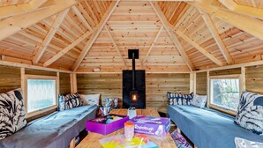 Interior acogedor de una cabaña con techo alto, paredes de madera, una chimenea central y dos sofás enfrentados.