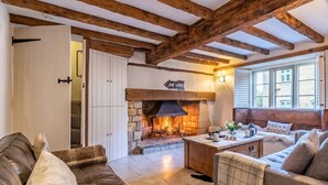 Ein gemütliches Wohnzimmer mit Kamin aus Stein, Holzbalken und bequemen Sitzmöglichkeiten.
