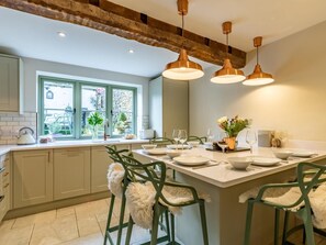 A modern kitchen with a large island, green chairs, pendant lighting, and a view through a window. - 3 Bed in Cheltenham (oc-49965) (Lower Swell)