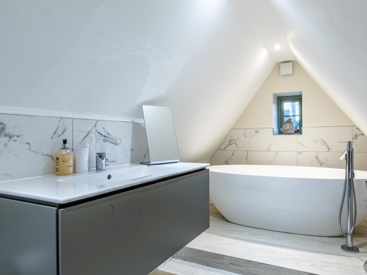 Een moderne badkamer met een vrijstaand bad, een grote spiegel en marmeren tegels.