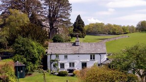 A white house with a grey roof, surrounded by greenery and a stone wall. - 4 Bed in Hawkshead (oc-llh02) (Near Sawrey)