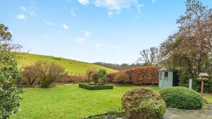 A garden with a stone pathway, a small shed, and a hill in the background. - 4 Bed in Hawkshead (oc-llh02) (Near Sawrey)