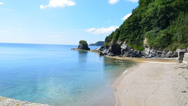A beach with clear water, a rocky outcrop, and a forested hillside. - 2 Bed in St. Austell (oc-50111) (Charlestown)