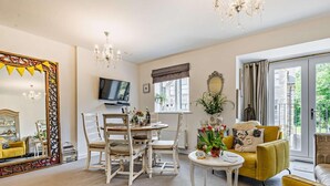 A living room with a dining table, chairs, a TV, a large mirror, and a yellow sofa. - 2 Bed in St. Austell (oc-50111) (Charlestown)