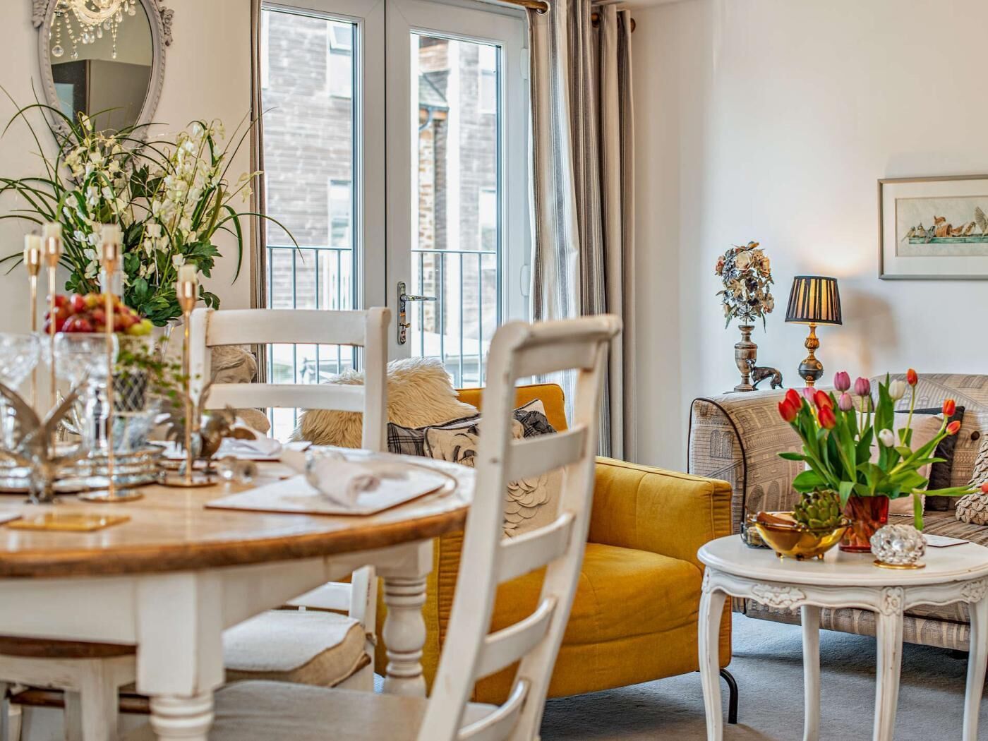 A dining area with a wooden table, white chairs, a yellow sofa, and a small white table with decorative items.