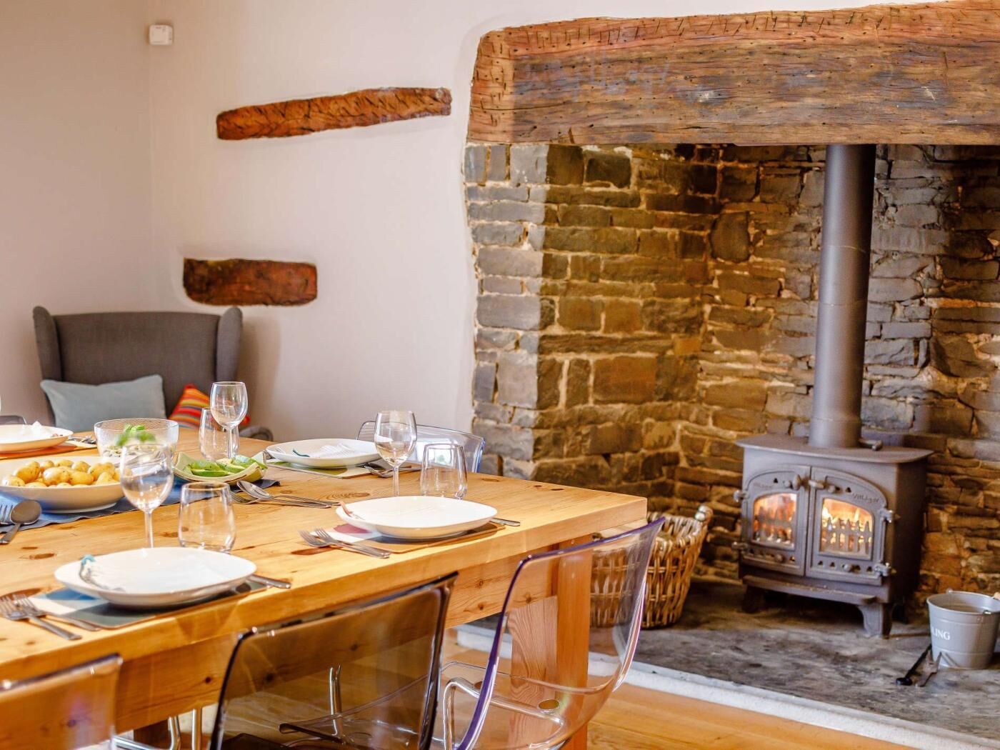 A dining area with a stone wall, a wooden table set for a meal, and a wood-burning stove.