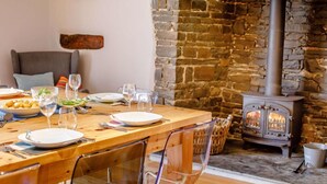 A dining area with a stone wall, a wooden table set for a meal, and a wood-burning stove. - 4 Bed in Umberleigh (oc-50154) (Burrington)