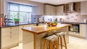A modern kitchen with a central island, bar stools, a window, and a built-in oven. - 4 Bed in Umberleigh (oc-50154) (Burrington)
