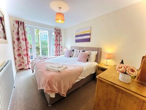 A bedroom with a bed, bedside tables, a radiator, a window with curtains, and a painting on the wall. - 1 Bed in Hawkshead (oc-llh16) (Hawkshead)