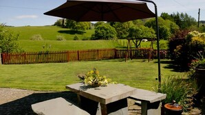 Eine Terrasse mit zwei Steintischen und einem Sonnenschirm, umgeben von einem Holzzaun und Grünpflanzen.