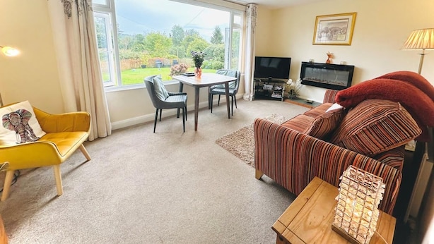 Ein Wohnzimmer mit einer Couch, einem gelben Sessel, einem Esstisch und einem Fernseher.