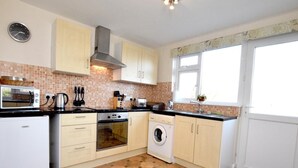 Eine Küche mit Mikrowelle, Backofen, Waschmaschine und gefliestem Spritzschutz.