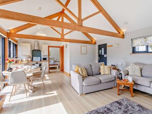 A spacious living area with a high ceiling, wooden beams, a sofa set, a dining table with chairs, and a kitchen in the background. - 1 Bed in Beaworthy (oc-50217) (Virginstowe)