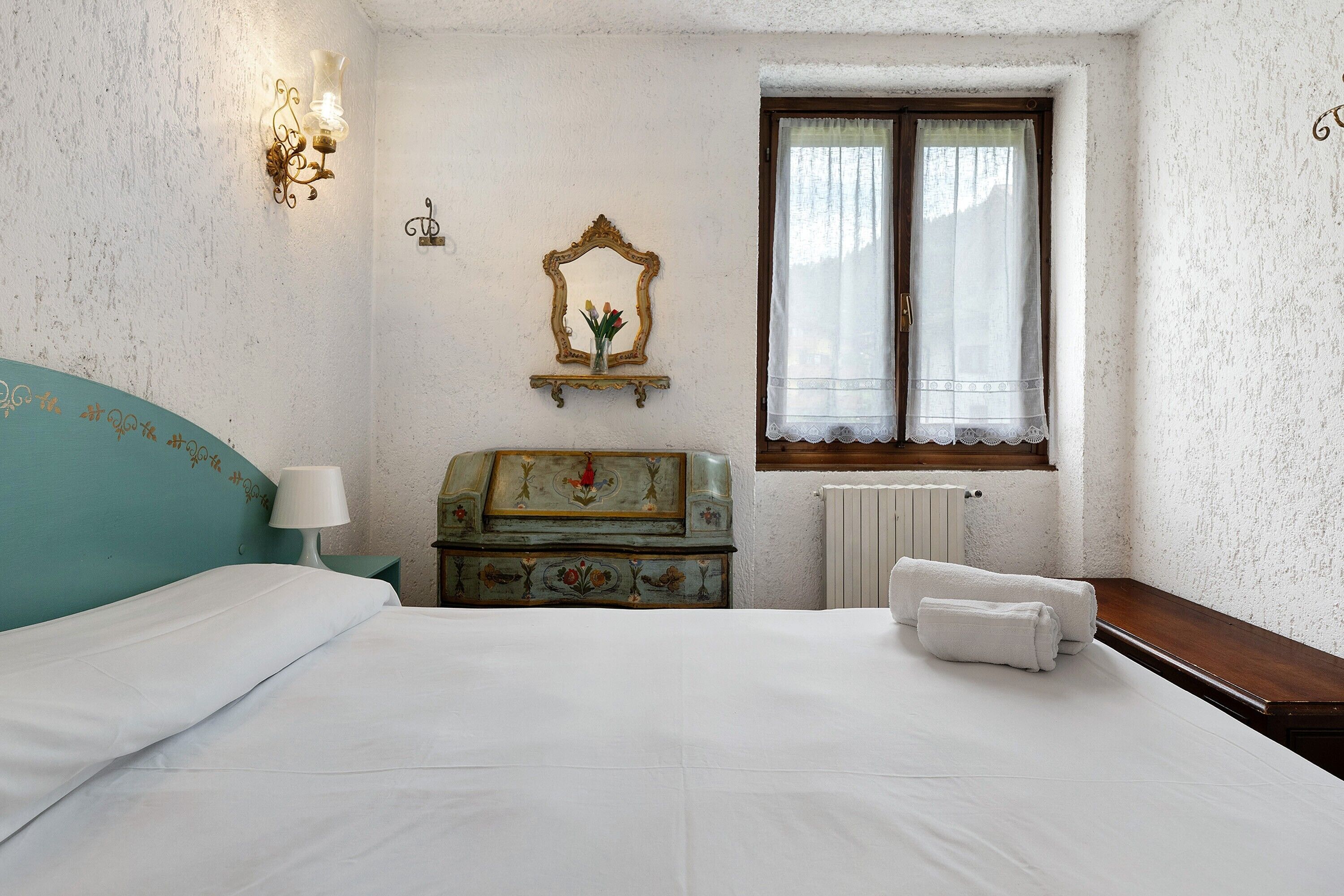 A bedroom with a bed, a nightstand, a dresser, a mirror, and a window with curtains.