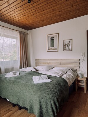 A bedroom with a wooden ceiling, a green quilted bedspread, white pillows, a wooden nightstand with a lamp, and two framed pictures on the wall. - Das Luis (Altenmarkt im Pongau)
