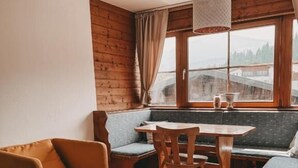 Ein gemütliches Zimmer mit Holzboden, einer Couch, einem Esstisch mit Stühlen und einem Fenster mit Vorhängen.