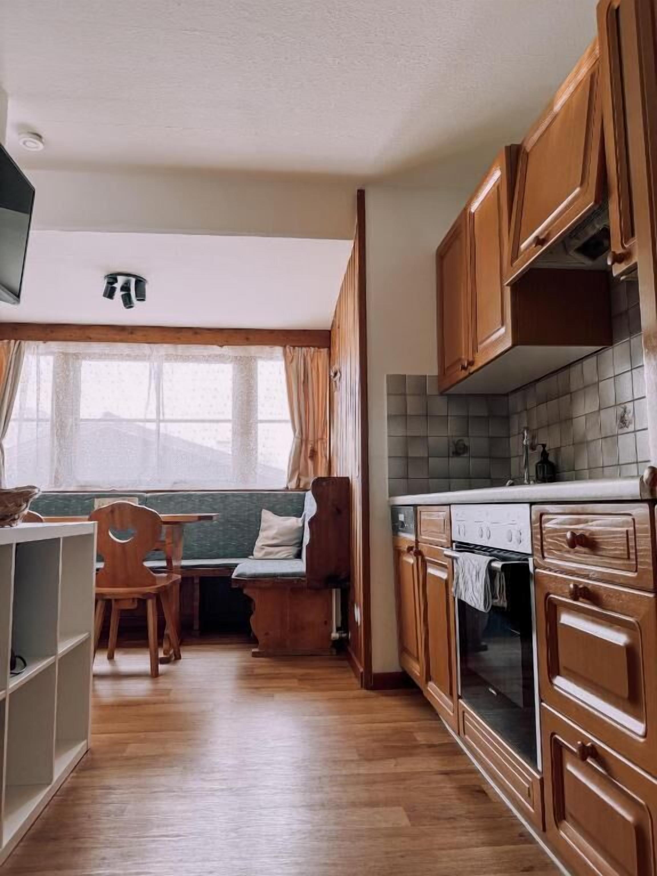 A kitchen with wooden cabinets, a dining area with a bench, and a window with curtains.