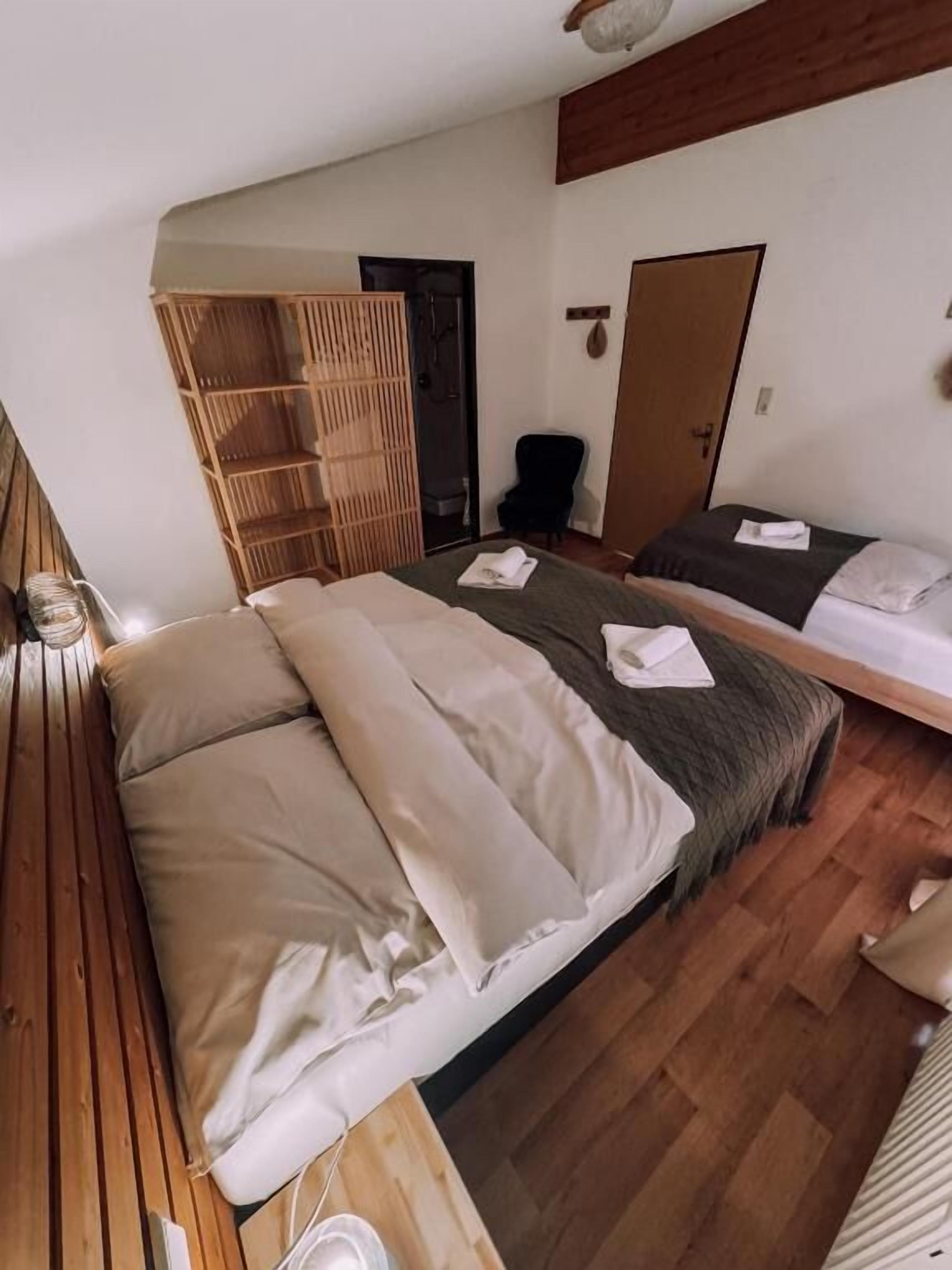 Une chambre avec un grand lit, un plus petit lit, une armoire en bois, une chaise et une porte.