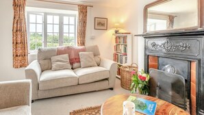 A cozy living room with a sofa, a fireplace, a bookshelf, and a window with curtains. - 3 Bed in Dorchester (oc-50290) (Hilfield)