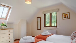 Un dormitorio con dos camas, un aparador, una ventana con vista a la vegetación e iluminación en el techo.
