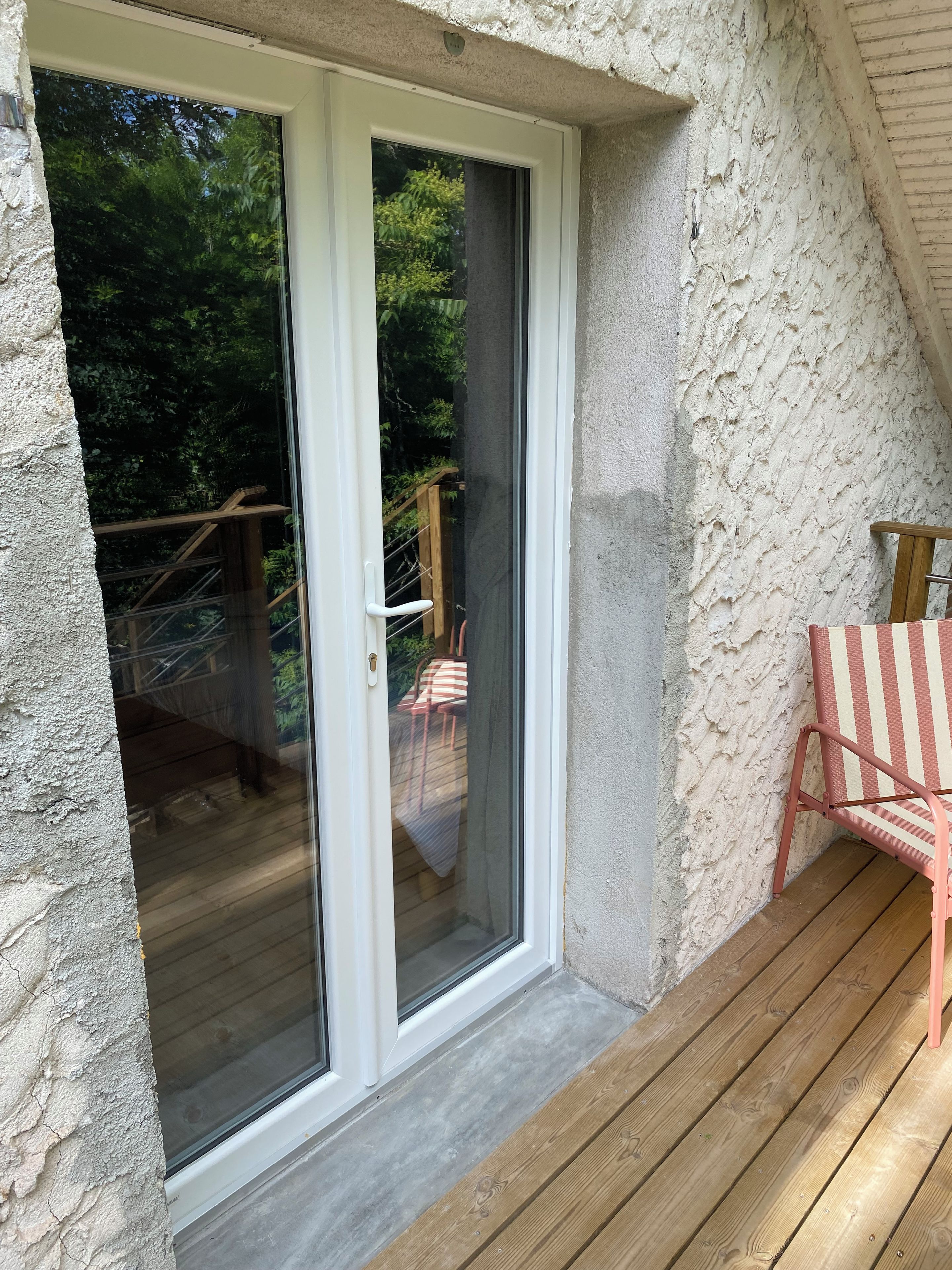 A wooden deck with a sliding glass door leading to a balcony with a view of greenery.
