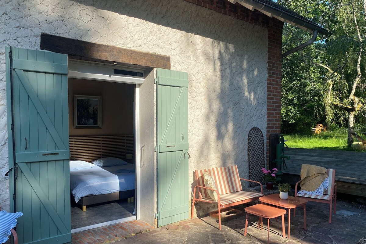 Una habitación con puerta abierta, una cama, una silla, una mesa y un pequeño jardín.