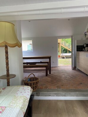A room with a bed, a table, a lamp, and a view of a wooden deck and outdoor area. - Maison joviale (La Ferté-Saint-Aubin)