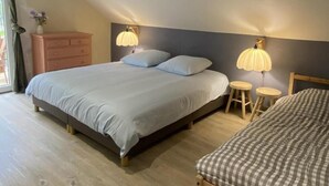 Un dormitorio con una cama grande, dos lámparas de noche, un taburete pequeño y un aparador.