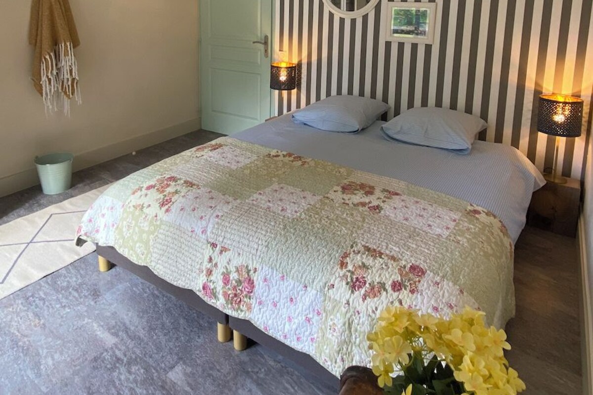 Un dormitorio con una cama, una puerta, un espejo montado en la pared y una pequeña fotografía.
