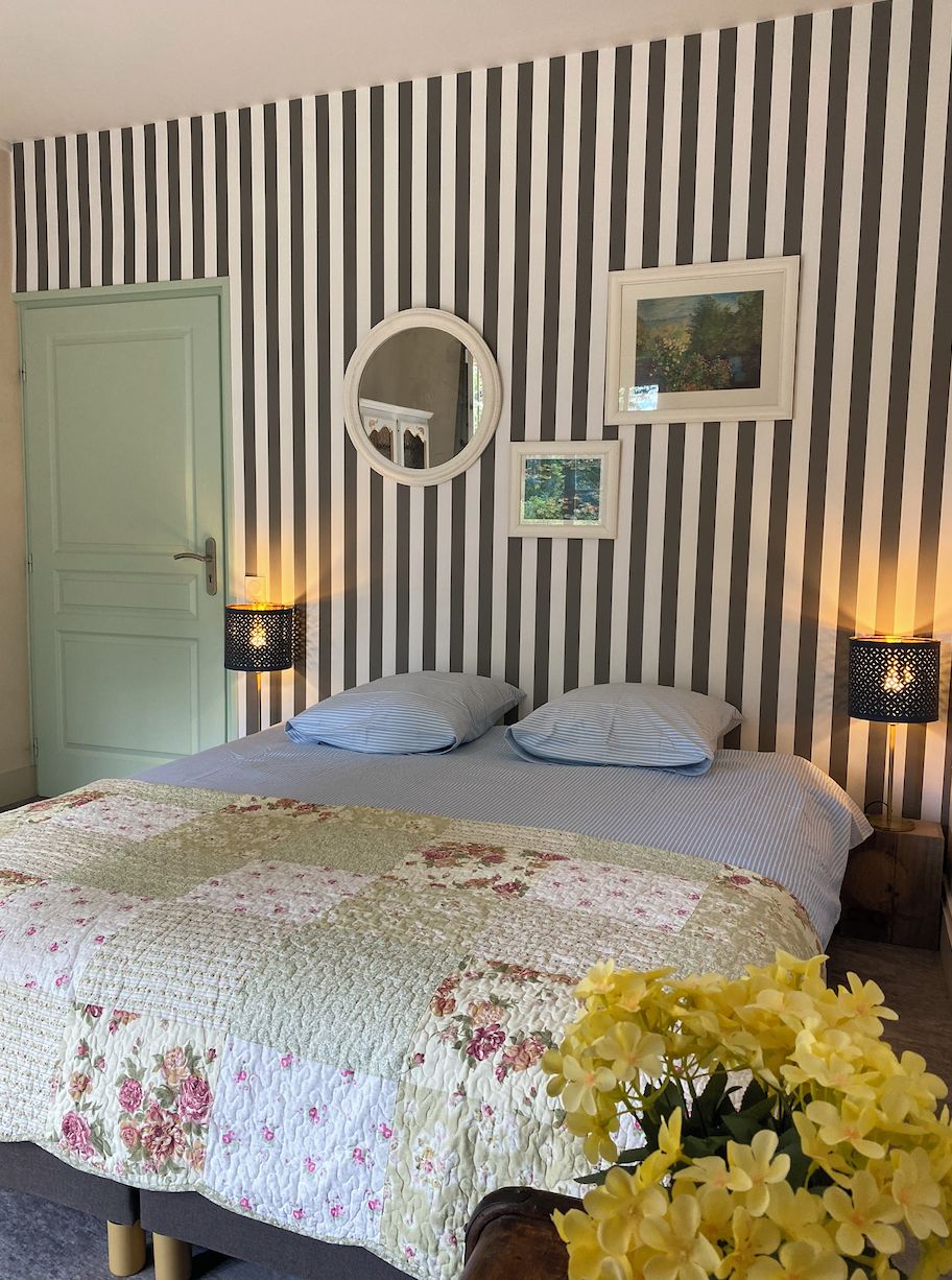 A bedroom with a bed, striped wallpaper, a door, a mirror, and wall-mounted lights.