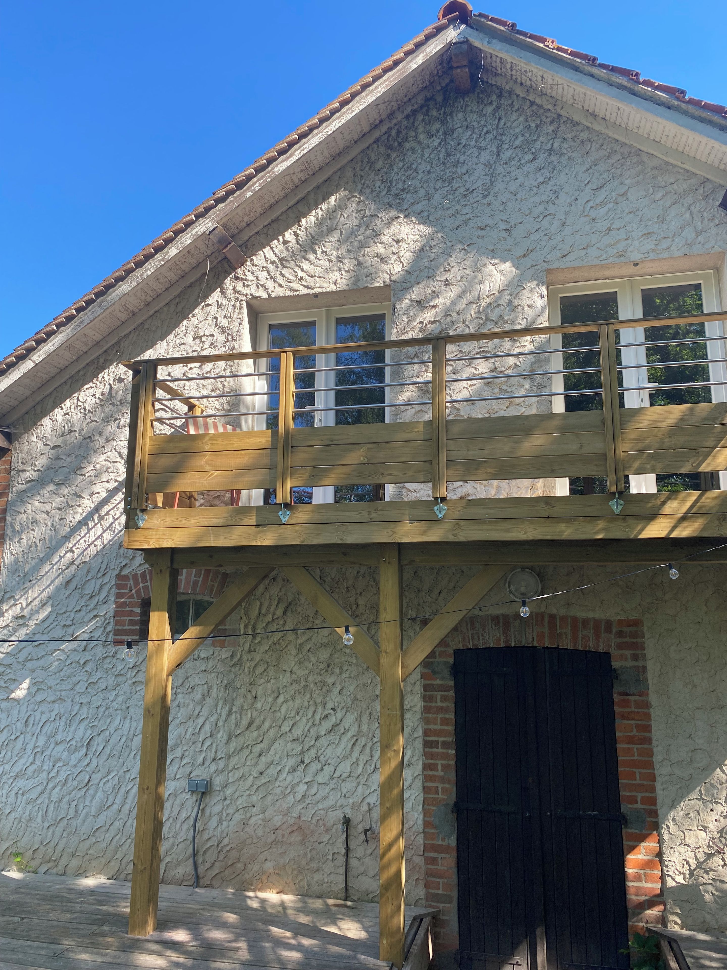 Un edificio de dos pisos con terraza de madera, entrada de ladrillo y fachada de piedra.