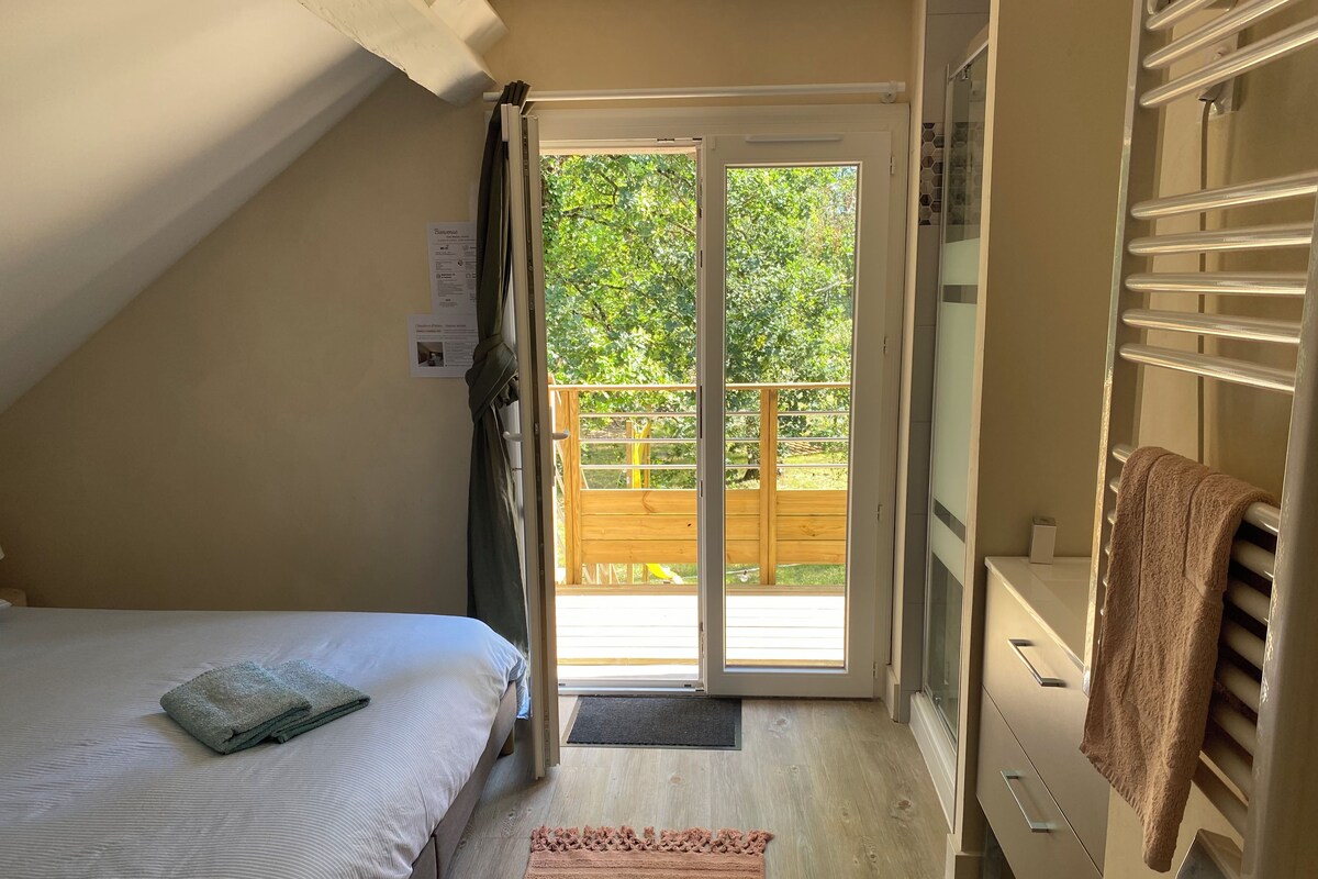 Un dormitorio con cama, piso de madera, puerta de cristal corredera que da a un balcón y un perchero para toallas.
