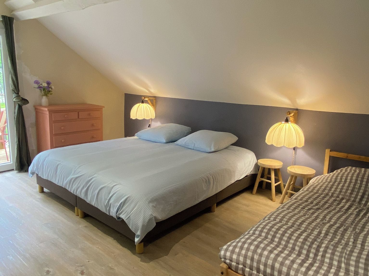 Un dormitorio con una cama grande, dos lámparas de noche, un taburete pequeño y un aparador.