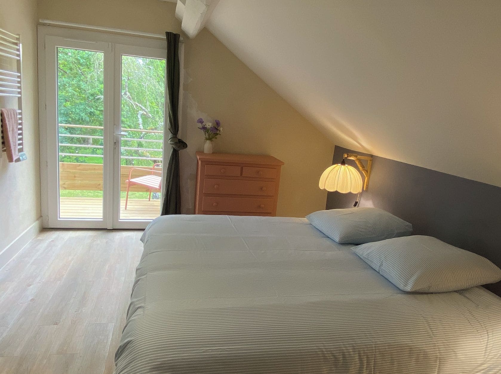 A bedroom with a bed, a dresser, a nightstand with a lamp, and a sliding glass door leading to an outdoor area.