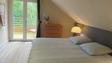 Une chambre à coucher comprenant un lit, une commode, une table de chevet avec une lampe et une porte-fenêtre coulissante donnant sur un espace extérieur.