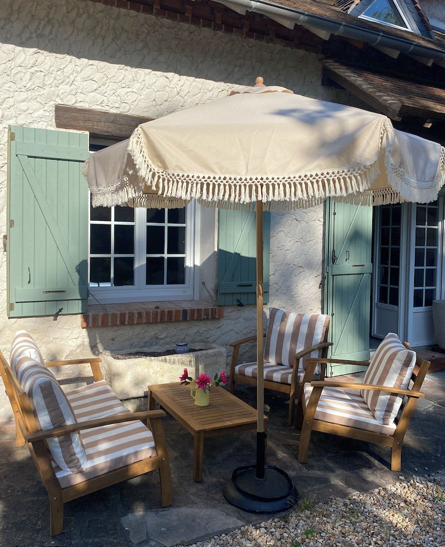 Uma área externa com mesas e cadeiras, um guarda-sol decorativo e um muro de pedra.