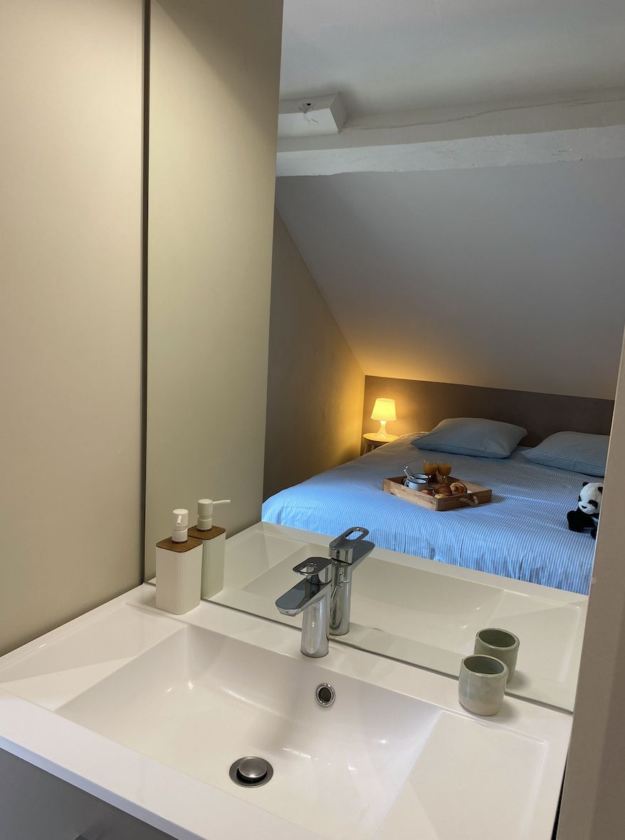 Un baño moderno con un espejo grande, un lavamanos y una mesita de noche con una lámpara y una bandeja con alimentos para el desayuno.