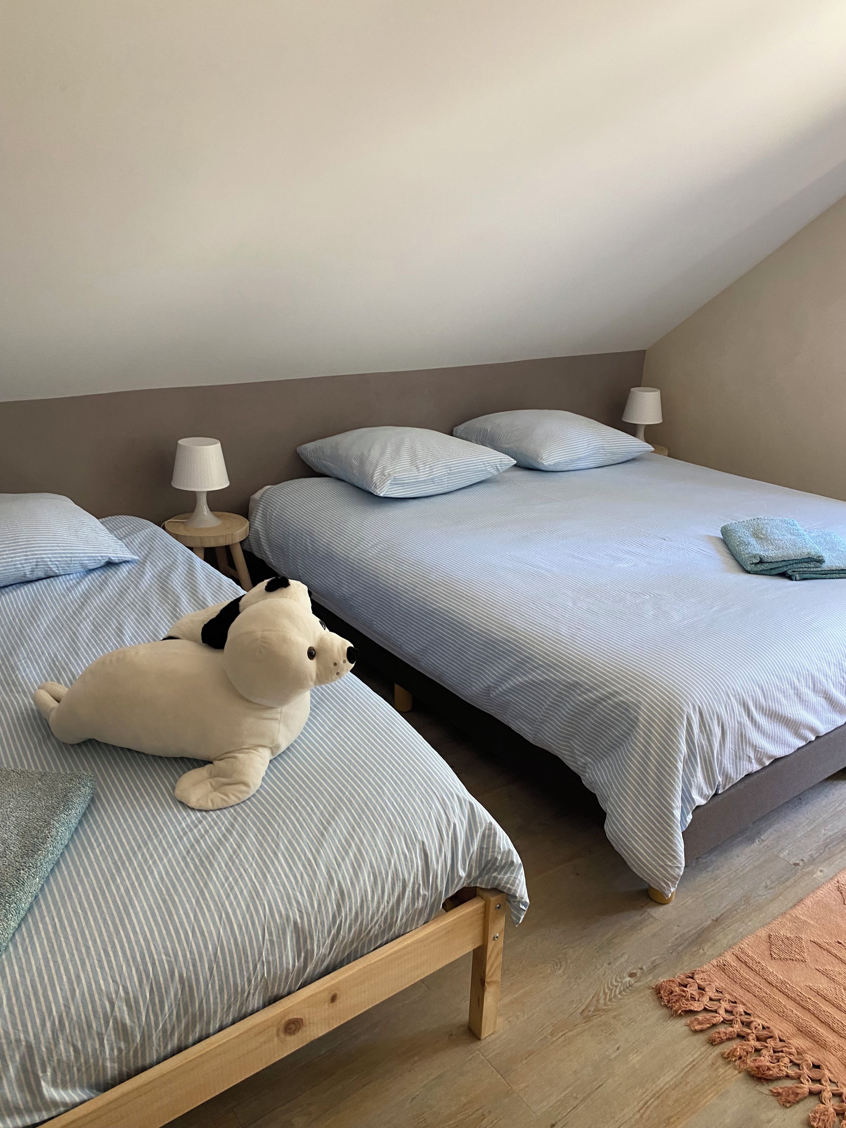 A bedroom with two beds, each with a striped bedspread, a small bedside table with a lamp, and a plush toy on one bed.